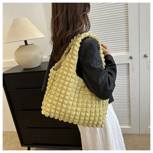 Detail of yellow puffer tote bag with bubble texture shown on female model's shoulder