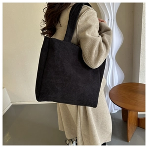 Detailed view of a black corduroy tote bag worn with a beige wool coat in a modern room