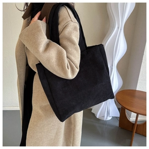 Close-up of black corduroy tote bag showing the vertical ribbed texture and shoulder straps