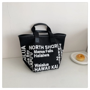 Close-up of black canvas tote bag with white Hawaii typography print in lifestyle setting