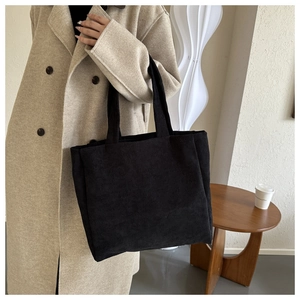 Detail of a large black corduroy tote bag styled with a beige coat in a minimalist setting