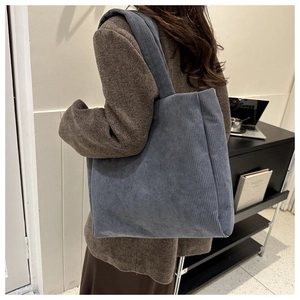 Detailed texture of blue striped corduroy tote bag worn by model in a cozy setting