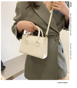 Close-up of a minimalist cream crossbody handbag held by a model in a green blazer