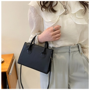 Detail of a minimalist black square tote bag with gold hardware and a slim shoulder strap