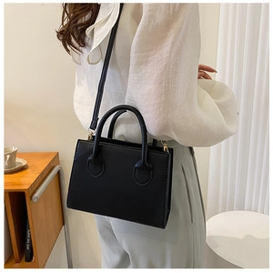 Minimalist black leather handbag with gold hardware shown in a lifestyle home setting