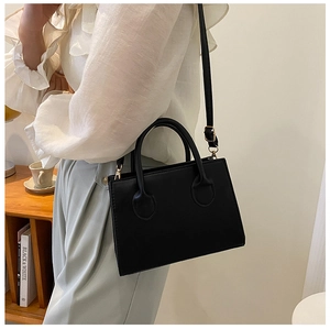 Detailed shot of black faux leather handbag with gold buckles and adjustable strap