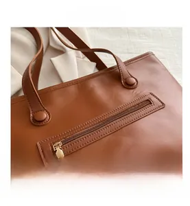 Dettaglio della borsa tote in pelle marrone con tasca zip e fibbie metalliche eleganti
