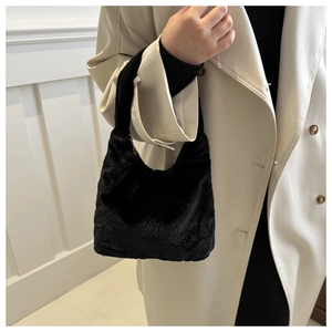 Détail d'un sac à main noir en peluche scintillante porté avec un manteau beige