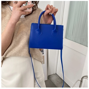 Model holding a vibrant royal blue square handbag with slim straps and sleek synthetic leather