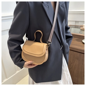 Detail of khaki saddle bag featuring smooth leather and striped wide crossbody strap