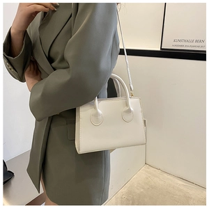 Close-up of a white minimalist handbag with round handle base on a grey-green blazer