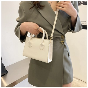 Detail of white minimalist crossbody bag with gold hardware on olive green suit