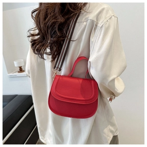 Close-up of red saddle bag featuring a wide striped fabric strap on a model outfit