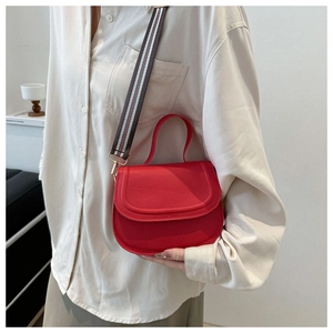 Close-up of red PU leather saddle bag with round handle and colorful striped strap