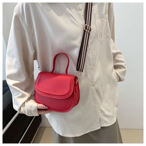 Red PU leather saddle bag detail with detachable striped wide strap shown on a model