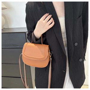 Brown leather saddle bag with striped strap shown on a model in a minimalist setting