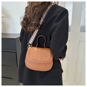 Detail view of a brown saddle bag featuring a wide colorful striped woven shoulder strap
