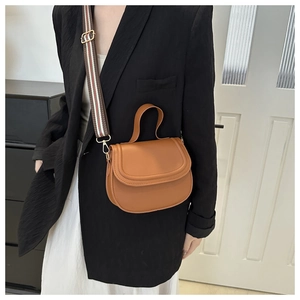 Brown saddle bag with striped strap and top handle shown on a model in a minimal room