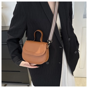 Brown faux leather saddle bag shown on shoulder with wide colorful strap detail