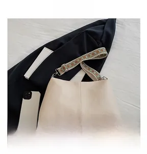 Detail view of beige lychee leather bucket bag with bohemian embroidered wide shoulder strap