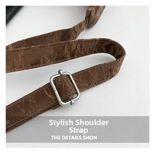 Détail d'une bandoulière marron texturée avec boucle de réglage en métal argenté