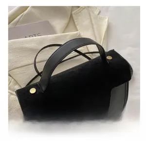 Detail of black handbag showing matte suede flap and smooth leather with gold accents