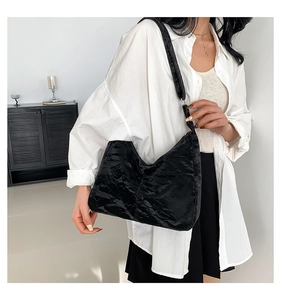 Gros plan d'un sac hobo noir à texture plissée porté à l'épaule par un mannequin