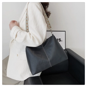 Detail of black pebbled leather tote with white stitching and geometric jacquard strap