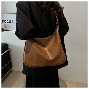Detail einer braunen Hobo-Tasche mit Faltenstruktur über einem schwarzen Mantel