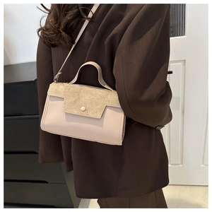 Detail of beige faux suede crossbody bag worn with a dark blazer in home setting