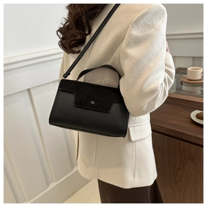 Detail of a black faux suede crossbody bag worn with a white tweed jacket