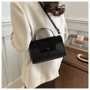 Detail of black faux suede and leather crossbody bag with gold hardware worn by model
