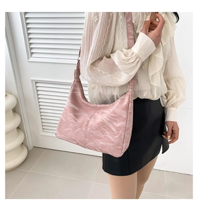 Détail du sac hobo rose en cuir verni froissé porté par un mannequin dans une pièce claire