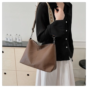 Brown vintage leather bucket bag with wide woven strap shown on model in cozy room