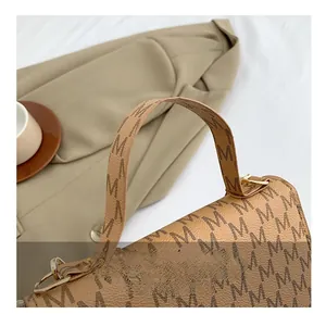 Detail of a brown leather handbag with M-pattern print and gold D-ring hardware
