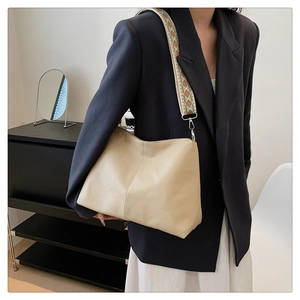 Close-up of beige leather tote bag with stylish colorful jacquard woven wide shoulder strap