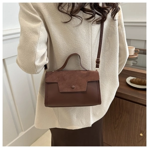 Detail of a dark brown suede and smooth leather retro shoulder bag worn by a model