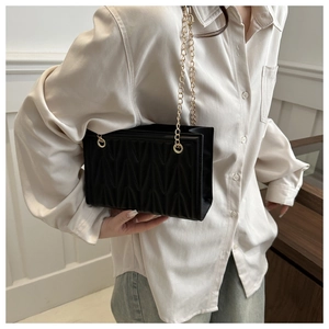 Detail of black quilted leather texture and gold chain strap on an elegant shoulder bag