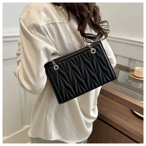 Detail of black matelassé leather shoulder bag with fine gold chain strap on a model