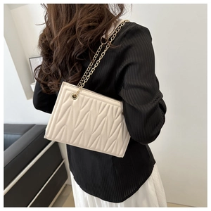Detailed view of beige pleated crossbody bag with gold chain strap on model's shoulder