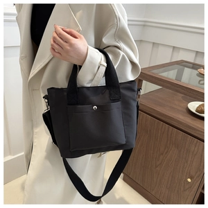 Close-up of black nylon tote bag featuring front pocket with silver metal snap and wide strap