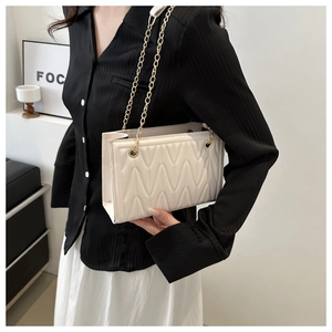 Detail of white quilted tote bag with wave texture and gold chain strap on model