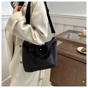 Detail of black nylon tote bag featuring a front pocket and adjustable wide shoulder strap