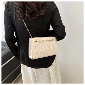 Chic beige quilted crossbody bag with wave texture and gold chain strap on shoulder