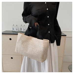 Detail of hand-woven straw tote bag with black strap handles for summer vacation