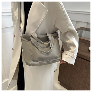Greyish green nylon tote bag shown as a crossbody bag on a model in a modern home interior