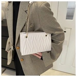 White quilted crossbody bag with gold chain strap worn over a khaki tailored blazer