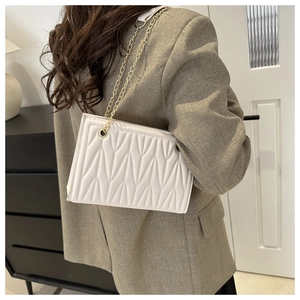Detail of white chain bag with geometric quilting and gold hardware on female model
