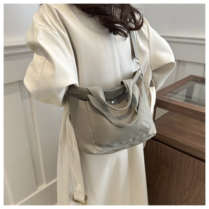 Back view of a grey large capacity nylon crossbody bag worn by a model in a cozy room