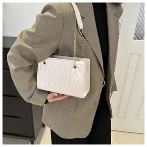 Detail of white quilted crossbody bag with gold chain strap worn on the shoulder